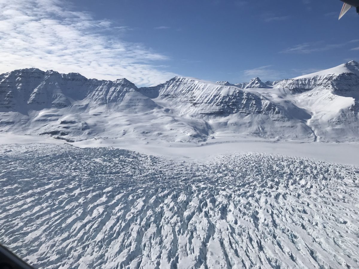 Photo of crevassed land ice in the foreground and Greenland mountains in the background.