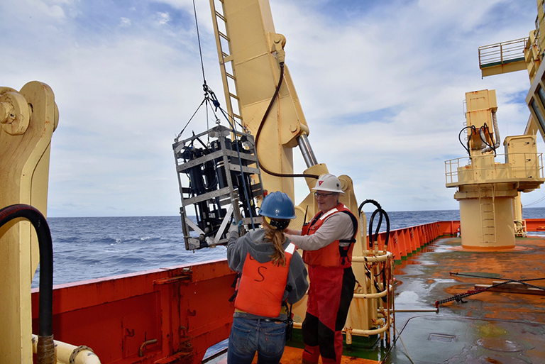 Crew members prepare an optical instrument for deployment over the side of the ship to collect optical measurements