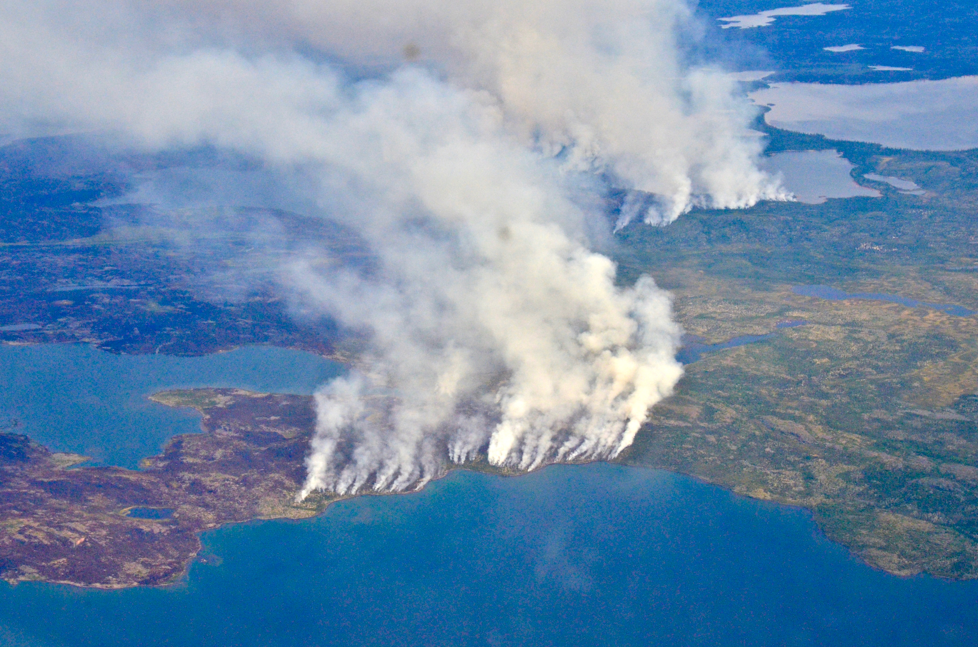 Large smoke plumes drift over land and ocean.