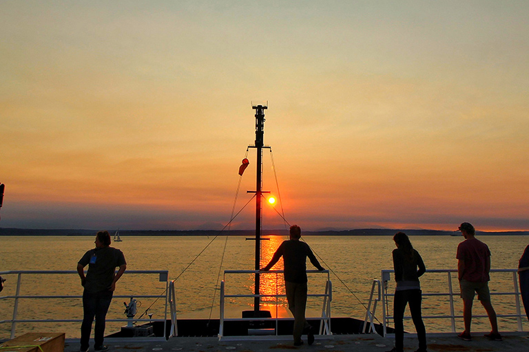 Scientists and crew aboard the Sally Ride watches the sunset as the ship leaves port in Seattle.