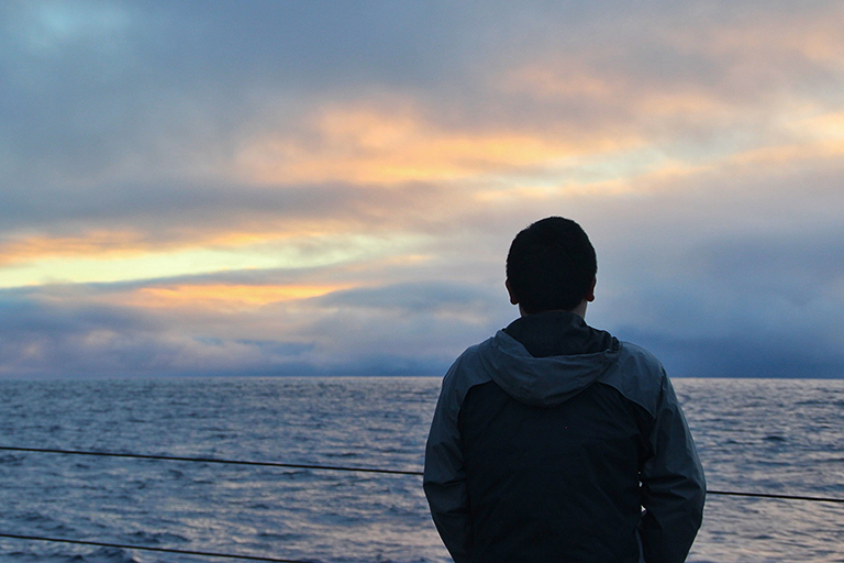 Yuanheng Xiong watches the sunrise from the back deck of the R/V Sally Ride.