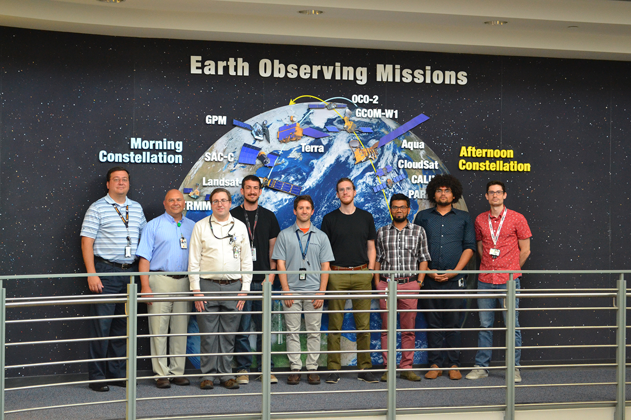 The offline Terra mission operations team stands in front of an image of the fleet of NASA Earth Observing Satellites.