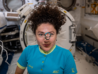 A female astronaut inside the International Space Station with a big drop of water floating in front of her face