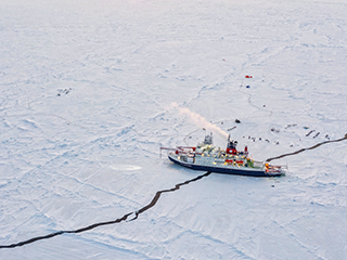 A boat called an icebreaker makes its way across Arctic sea ice.