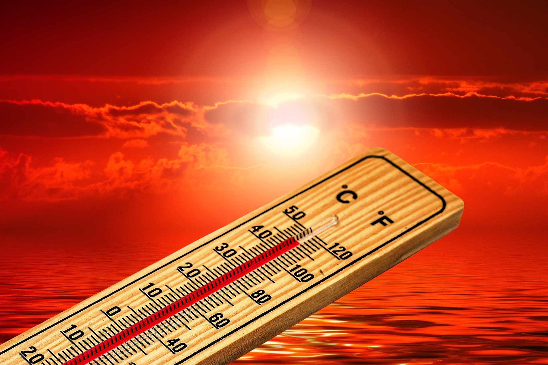 Thermometer with high, hot temperatures over an reddish-orange sunset sky and water.