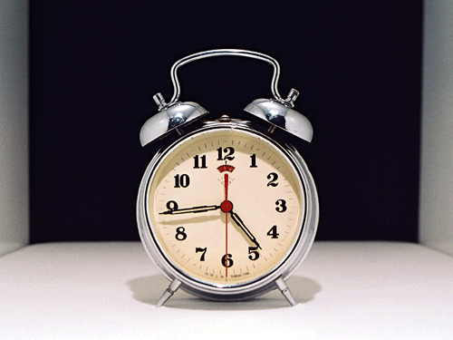 Silver alarm clock with two bells on the top and a black background.