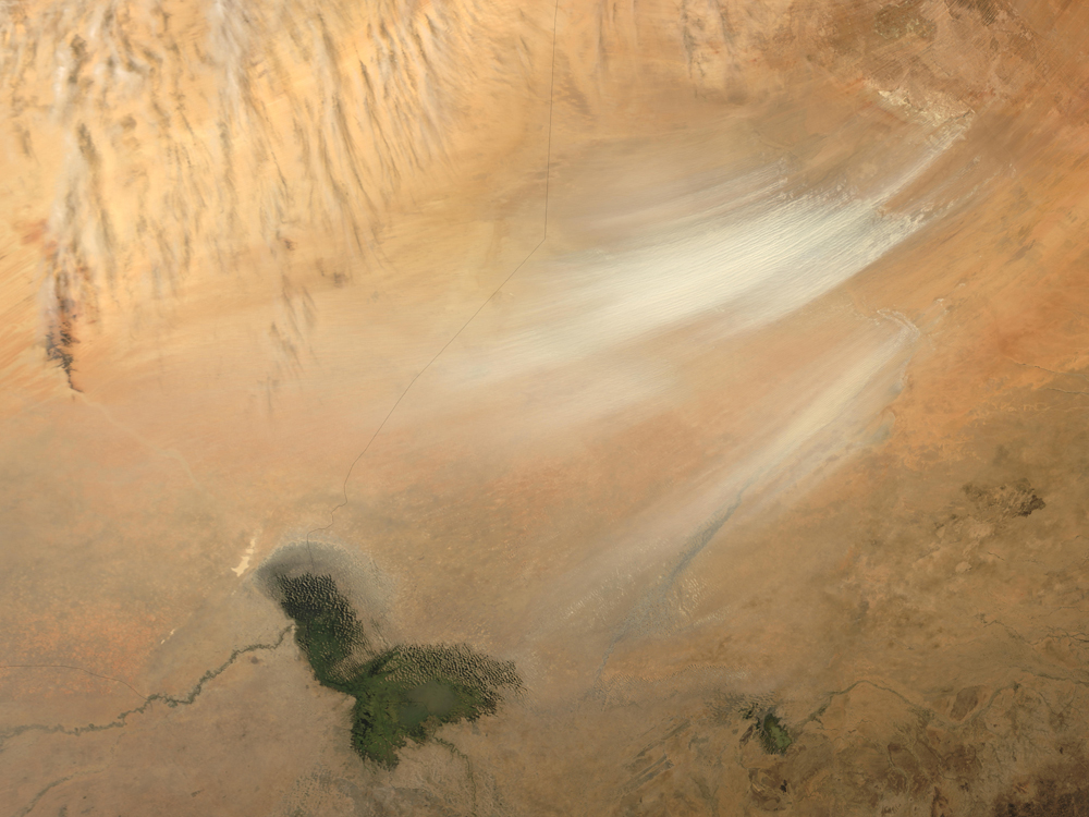 Lake Chad, Africa; February 7 and 11, 2004. Once serving as part of the floor for a much larger Lake Chad, the area now known as the Bodele Depression, located at the southern edge of the Sahara Desert in north central Africa, is slowly being transformed into a desert landscape. In the mid-1960s, Lake Chad was about the size of Lake Erie. But persistent drought conditions, coupled with increased demand for freshwater for irrigation, have reduced Lake Chad to about 5 percent of its former size. As the waters receded, the silts and sediments resting on the lakebed were left to dry in the scorching African sun. The small grains of the silty sand are easily swept up by the strong wind gusts that occasionally blow over the region. Once heaved aloft, the Bodeledust can be carried for hundreds or even thousands of kilometers.
The remnants of Lake Chad appear in olive-green amid the tan and light brown hues of the surrounding landscape where the countries of Chad, Niger, Nigeria and Cameroon all share borders. The Bodele Depression was the source of some very impressive dust storms that swept over West Africa and the Cape Verde Islands in February 2004, the date of this image.