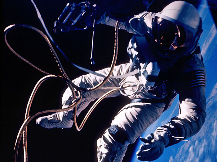 The United States' first spacewalk, made by Ed White on June 3, 1965 during the Gemini 4 mission. On the third orbit, White opened his hatch and used a hand-held manuevering oxygen-jet gun to push himself out of the capsule. After the first three minutes the fuel ran out and White manuevered by twisting his body and pulling on the tether. His extra-vehicular activity started over the Pacific Ocean near Hawaii and lasted 23 minutes, ending over the Gulf of Mexico. The photograph was taken by commander James McDivitt.