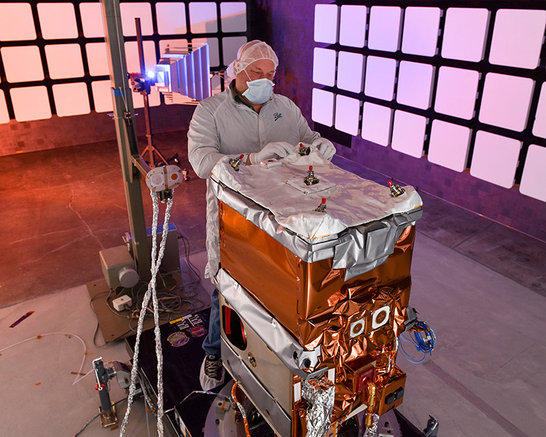 A Ball Aerospace engineer adjusts the thermal insulation on NASA’s Green Propellant Infusion Mission spacecraft bus following integration of the propulsion system. Credit: Ball Aerospace