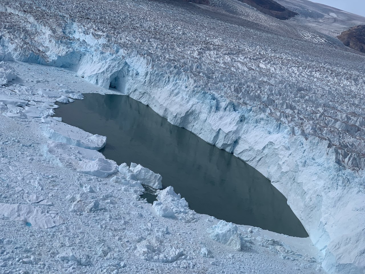 A large pool of open water at the edge of Helheim Glacier in east Greenland, as seen from the Oceans Melting Greenland (OMG) aircraft. The OMG team successfully dropped an ocean probe in this pool of water and measured the water temperature right at the glacier's face.