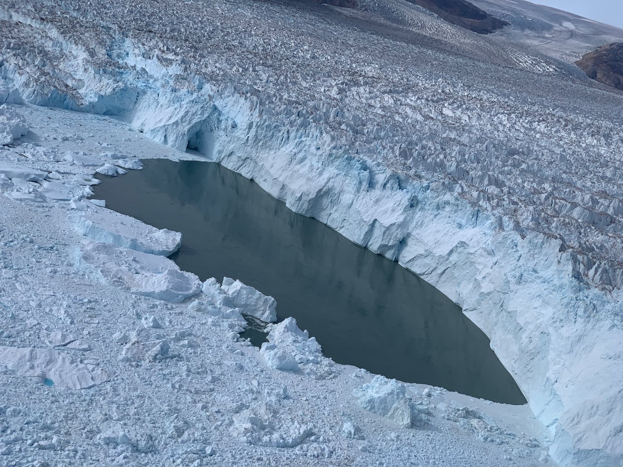 Uma grande piscina de águas abertas na borda da Geleira Helheim, no leste da Groenlândia, como vista da aeronave Oceans Melting Greenland (OMG). A equipe OMG derrubou com sucesso uma sonda oceânica nesta poça de água e mediu a temperatura da água bem na face da geleira.