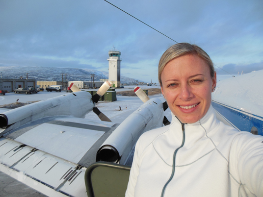 Christy Hansen in Kanger, Greenland, after one of Operation IceBridge’s science flights. Behind her is the air traffic control tower, as well as the P-3B propellers. Credit: Christy Hansen