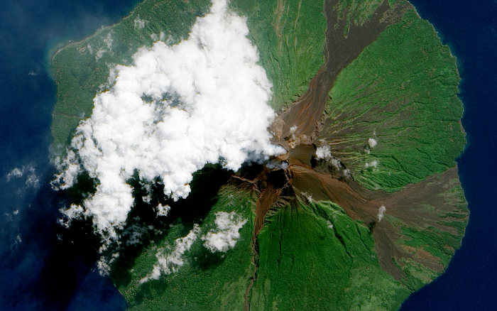 MANAM VOLCANO: Manam Volcano in Papua New Guinea, as seen from space on June 16, 2010. Located 13 kilometers (8 miles) off the coast of mainland Papua New Guinea, Manam forms an island 10 kilometers (6 miles) wide. It is a stratovolcano. The volcano has two summit craters, and although both are active, most historical eruptions have arisen from the southern crater.
On June 16, the volcano released a thin, faint plume as clouds clustered at the volcano's summit. Rivulets of brown rock interrupt the carpet of green vegetation on the volcano’s slopes. White clouds partially obscure the satellite’s view of Manam. The clouds may be the result of water vapor from the volcano, but they may also have formed independently of volcanic activity. The volcanic plume appears as a thin blue-gray veil extending toward the northwest over the Bismarck Sea.
